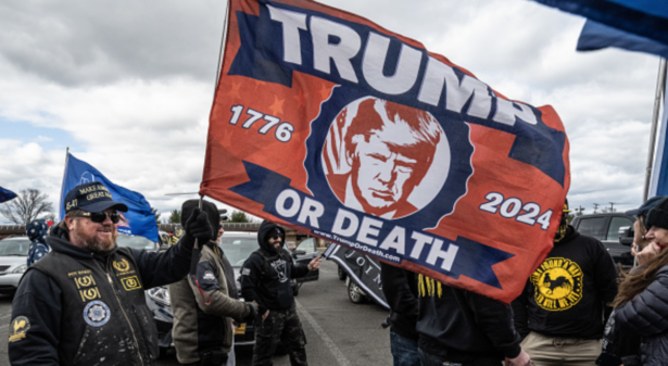 Proud Boys hols flag with text "Trump or Death"